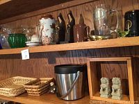 Shelf with various vases, ceramic and glass beer steins, monk bookends, woven baskets and an ice bucket.