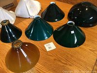 Ten various glass shades in brown, green, and black colors in conical and dome shapes arranged on a wooden surface.