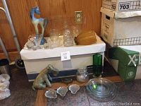 Various cut glass decanters, dog figurine, horse figurine, lamp shade, small dishes, and turtle figurine on box and counter.