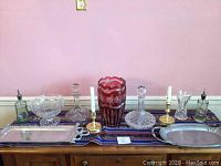 Full lot overview showing two decanters, tall red vase, candlesticks, trays, and table runner on wooden sideboard.