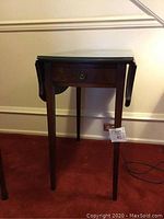 Small mahogany half moon occasional table with a single drawer, featuring slight scratches on legs. Glass top protection visible.