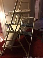 Three ladders standing side by side: one white Cosco ladder with plastic steps, a Werner ladder with paint on steps, and a smaller black-stepped Cosco ladder.