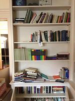 Wide view of full bookshelf showing assorted books and journals including stacked ones and color-coded journals