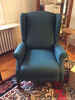 Single forest green wing back chair front view showing upholstery and wooden legs on patterned rug.