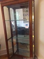 Full front view of tall, wooden framed display cabinet with three glass shelves and mirrored back.