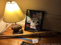 Photo showing signed Mickey Mantle picture plaque, football-themed desk lamp, and Louisville Slugger baseball bat on a wooden table.