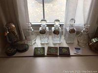 Full display of four decanters, three cut glass and one clear eagle etched, coaster tiles, metal coasters, and decorative tin box.