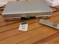 Front view of silver Insignia player showing display, disc tray, control buttons, remote control beside device.