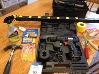 Photo showing True Value cordless drill in case with charger and assorted tools including hammer, sliding pads, Goo Gone spray, masking tape, Rug Gripper, and various hardware items.