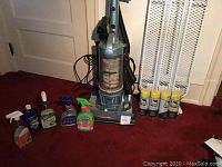 Photo of Fantom upright vacuum cleaner with cord and clear canister, four cans of Niagara starch, and various cleaning bottles lined up on red carpet.