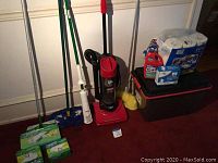 Photo showing Dirt Devil upright vacuum, yarn mop, long duster, Swiffer mop with new cloths, Latch Pro tote with assorted cleaning items, toilet paper and carpet cleaner packs on floor.