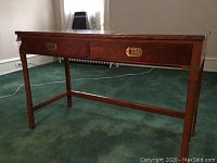 Front and side view of wooden desk showing two drawers and carved legs on green carpet.
