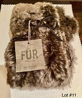 Full view of the tightly folded faux mink fur scarf with brand tag and leather cord visible.
