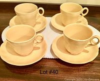 Four yellow/beige tea cups each paired with a matching saucer, styled with a scalloped petal edge on saucers, set on wooden surface.