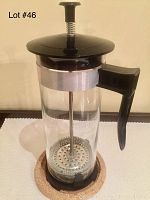 Front view of French press coffee maker showing glass carafe, black plastic handle, lid, and base with metal plunger inside.