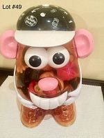 Large translucent plastic Mr. Potato Head storage container with black and white baseball cap lid and attached ears, showing front face with eyes, nose, and mouth inside.