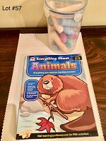 Photo showing the Everything About Animals workbook placed on a wooden surface with a plastic container of multicolored chalk beside it.