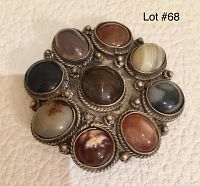 Front view of vintage circular pin brooch with ten oval cabochon stones in assorted earth tones set in metal with rope and bead details.