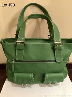 Front view of green Joan Rivers tote bag showing zippered front pocket, flap pockets, handles, and silver buckles.