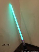 Star Wars lightsaber toy glowing green blade turned on, leaning against wall.