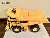 Side view of yellow Caterpillar toy dump truck with large black wheels and empty dump bed on a white textured mat