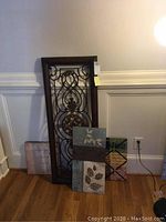 Three pieces of wall art leaned against a wall including the large metal wall art piece and two canvas art pieces.