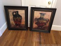 Pair of framed paintings depicting vases, both signed by N. Wyatt Jr., displayed leaning against a wall