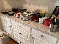 Wide view of countertop with various dishes including Pfaltzgraff Aster pattern sets, mugs, a thermos, and other serving items.