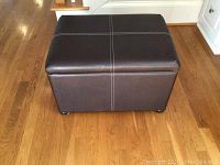 Photo of the closed dark brown faux leather ottoman showing the white stitched cross pattern on top and the textured surface.