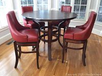 Four red bar stools arranged around a round table on hardwood floor