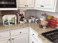 Countertop view showing boxed Anchor Hocking glassware set, Gibson mug set with holder, and assorted glass and plastic kitchen storage containers including Pyrex pieces.