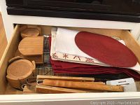 Drawer open showing wooden coasters sets, wooden napkin holder, metal racks, and fabric placemats stacked inside.