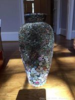 Single large vase covered in colorful rolled paper pieces on wooden floor near doorway
