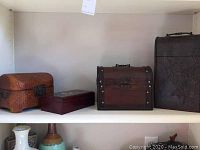 Shelf with four decorative boxes of various types including a woven texture box, wood jewelry box, curved wood box, and metal wine box.