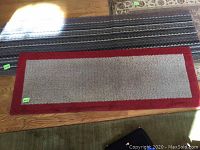 Rug with red border showing its full length and edging detail, placed on wooden floor.