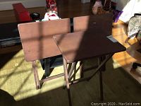 Two wooden TV trays folded open side by side on floor in sunlight, showing structure and size.