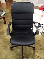 Full view of black office chair showing padded armrests, high backrest with segmented stitching, leather and mesh fabric upholstery, and five wheel base.