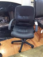 Full view of black swivel office chair showing padded seat and backrest, arm supports, and base with wheels on hardwood flooring.