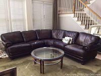 Full view of L-shaped dark brown leather sectional sofa and round glass coffee table.