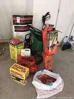 Wide shot showing all items: boxed pressure washer, spreader, hedge trimmer box, sprayer, extension cords, gloves and deer repellent.