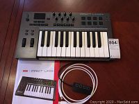 Full view of Nektar Impact LX25plus keyboard controller with USB hub and cable laid out, along with the user manual on wooden floor.