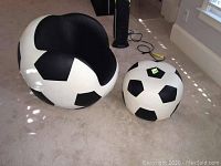 Full view of child's soccer ball themed chair and matching ottoman on carpet. Chair shows round black and white pattern, cushioned black interior, ottoman matching design.