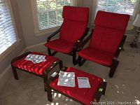 Pair of IKEA Poang chairs with red cushions and two matching ottomans, showing full set from front angle with instruction manuals on ottomans