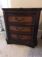 Front view of dark wood nightstand showing three drawers with metal handles