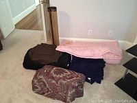 Several folded blankets, sheets, and a pink wool quilt on the floor