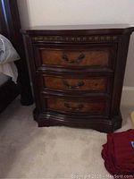 Front view of dark wood nightstand showing three drawers and carved molding