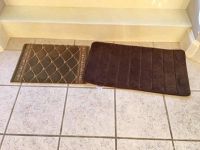 Two bath mats placed side by side on tiled floor, showing different designs and sizes.
