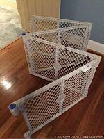 White plastic play yard panels folded in an accordion style on wooden floor.