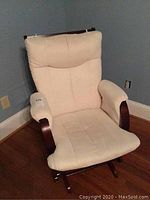 Full view of cream upholstered glider rocker chair showing chair back, seat, armrests, and wooden frame.