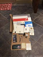 Full view of 22 art supplies items laid out on floor showing watercolor papers, pads, inks, tools, pastel and charcoal sets.